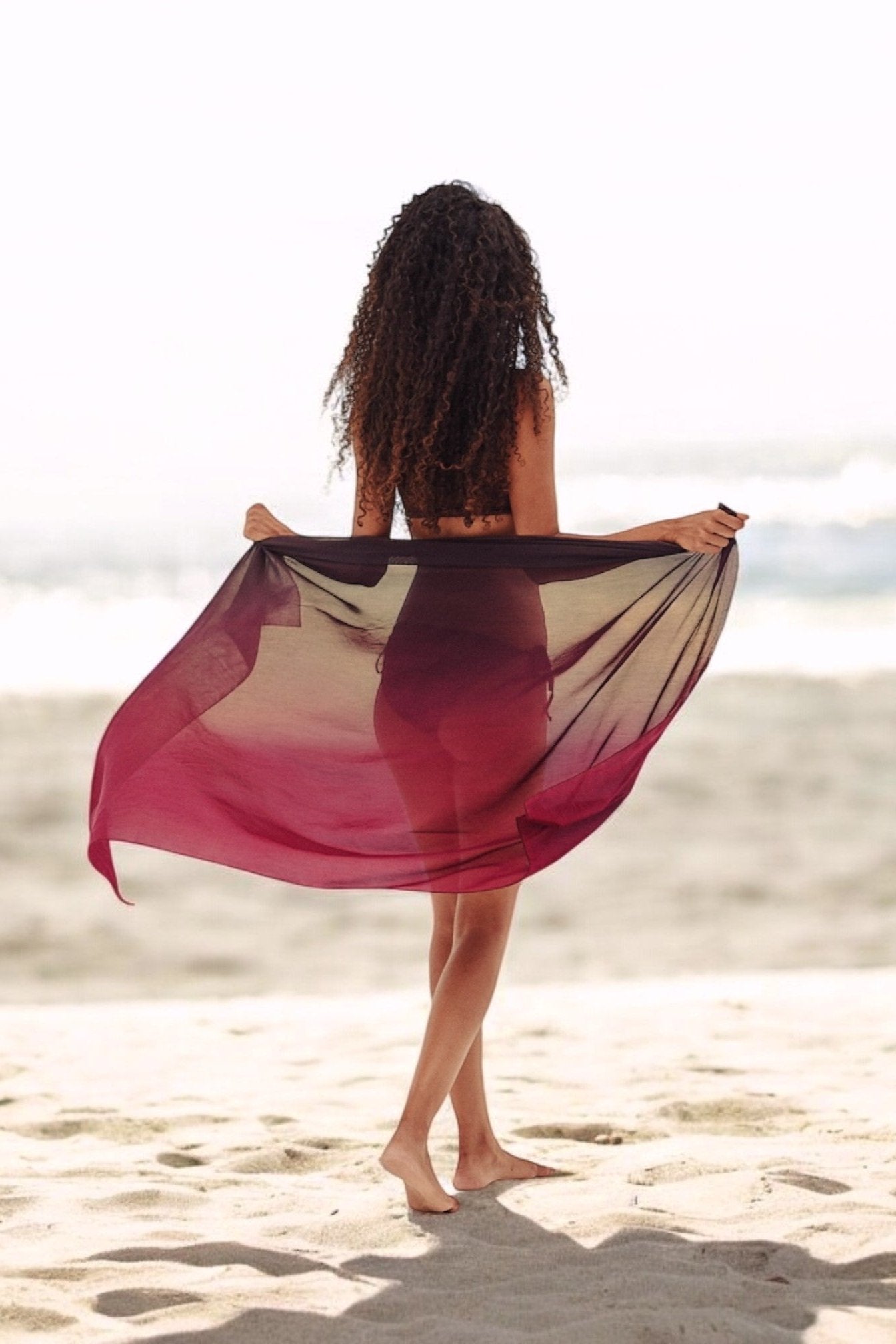 A person standing on a beach wearing a purple silk sarong draped around the waist.