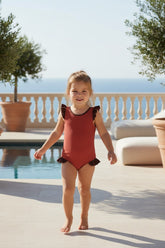Young girl in a red swimsuit standing by a pool with a scenic background