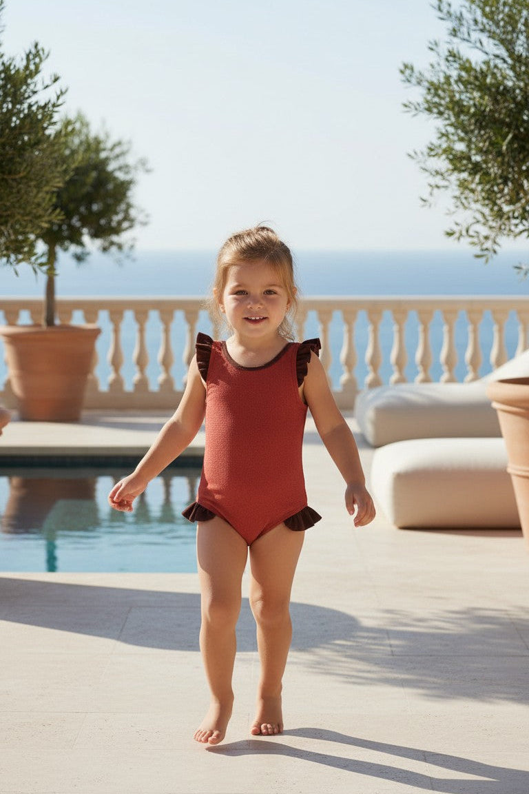 Young girl in a red swimsuit standing by a pool with a scenic background