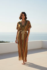 Woman in a patterned dress standing on a rooftop with a clear sky.
