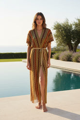 Woman in a patterned dress standing by a pool with greenery in the background