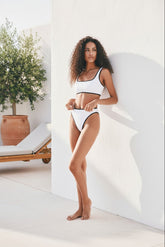 Woman in a white bikini standing in a bright, minimalistic outdoor setting.