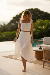 Woman in a white outfit standing on a patio with greenery and a pool in the background