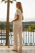 Woman in a white outfit standing on a balcony with palm trees and a pool in the background