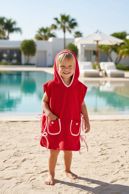 Child wearing a red hooded towel by a poolside with palm trees in the background