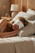 Woman sleeping in bed with a sleep mask on, wearing a nightgown.